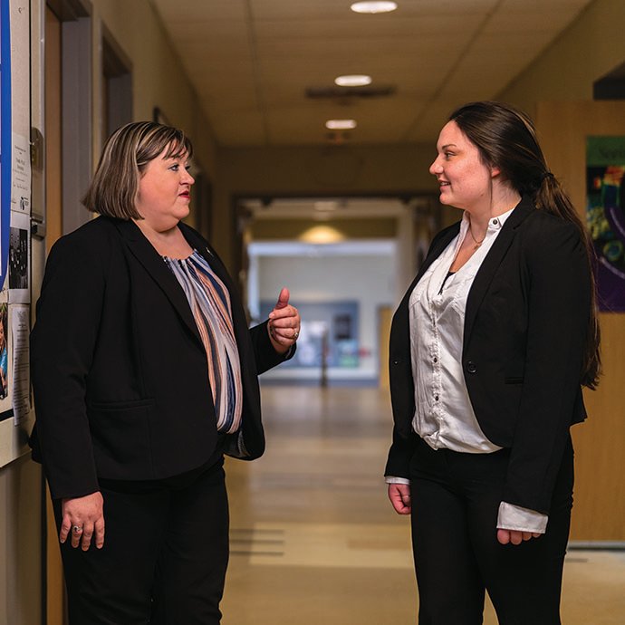 Female mentor and female student stand together in building hallway