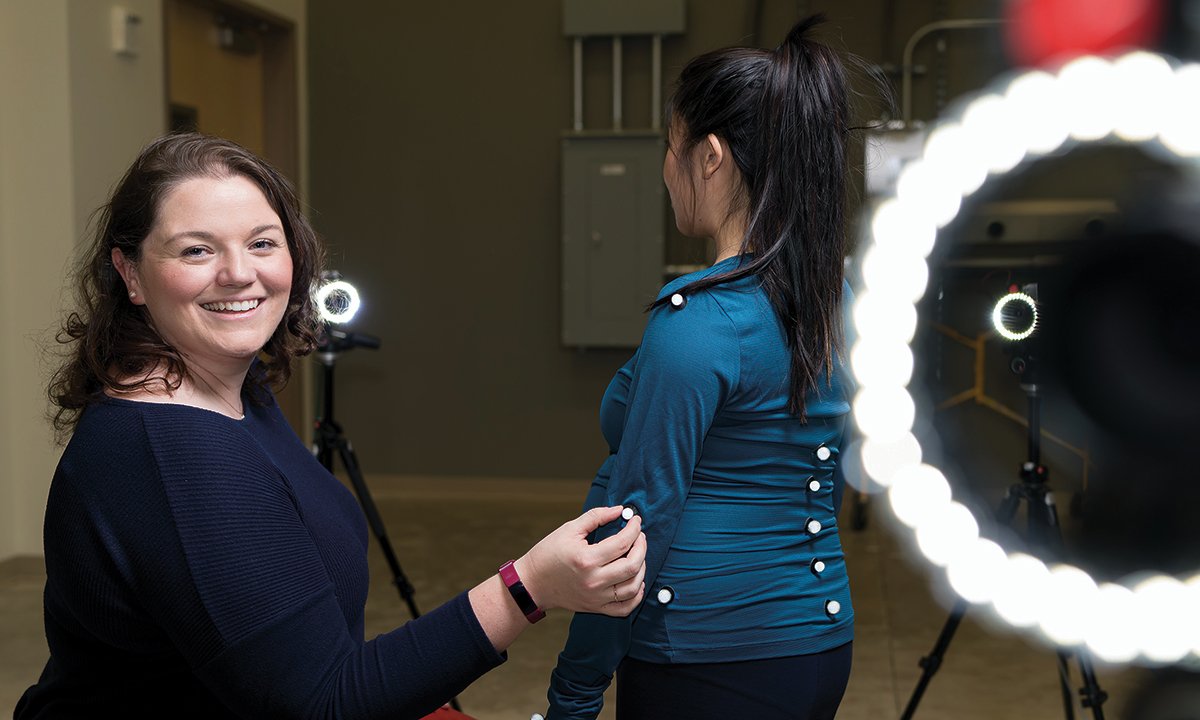 A woman smiling into the camera, standing next to a woman with her back to the camera