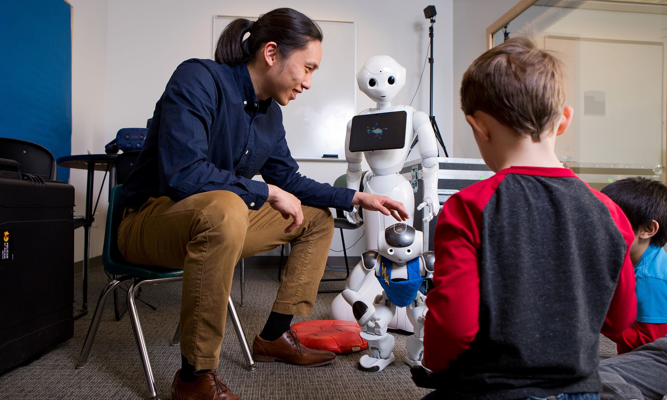 Man sitting on chair showing robots to two children