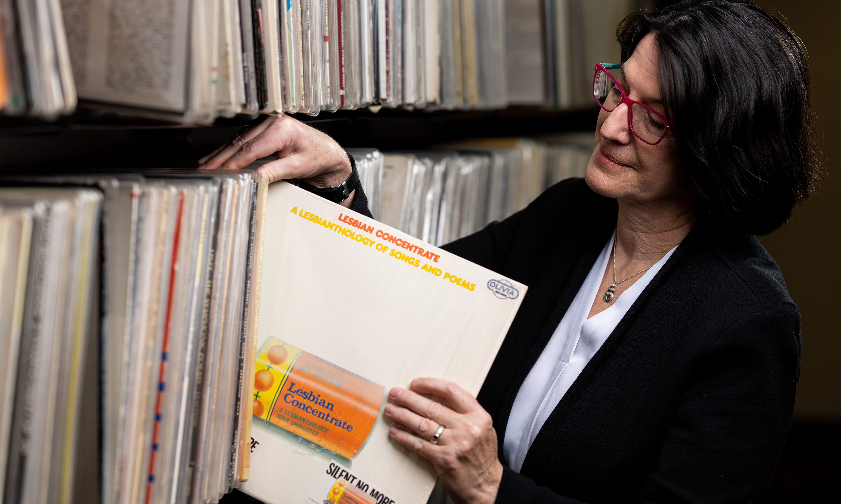 Woman pulling record album out of shelf of albums - record labelled "Lesbian Concentrate"