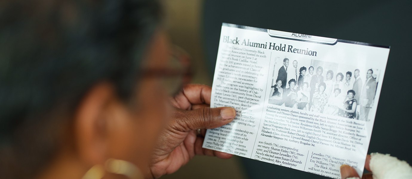 Woman holding photo of article with heading "Black Alumni Reunion"