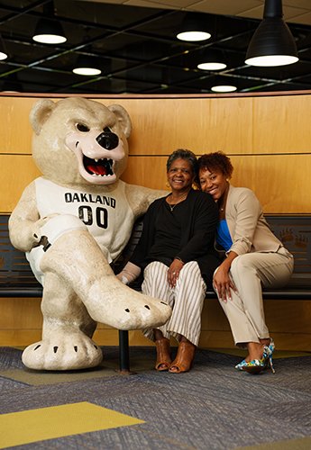 Two women sitting together next to bear mascot