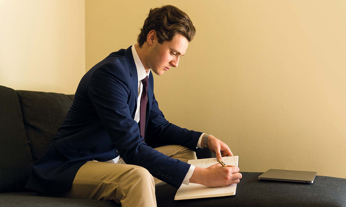 Male student sitting on chair writing in notebook