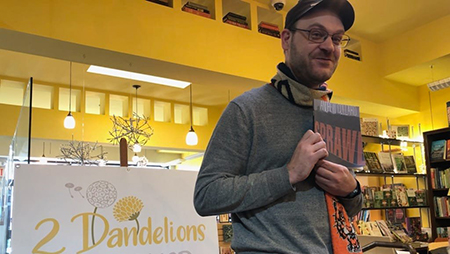 Andrew Collard holds up his book Sprawl inside a bookstore.