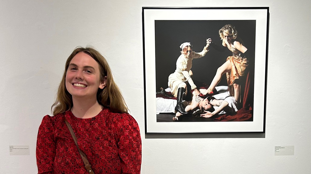 Photography student Courtney Blackett poses for a photo next to her version of “Judith Beheading Holofernes” (inspired by Artemisia Gentilschi)