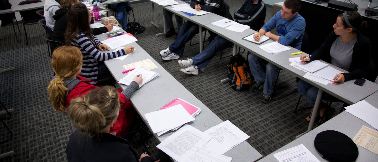 Students seated at tables situated in a rectangular shape, writing in notebooks.