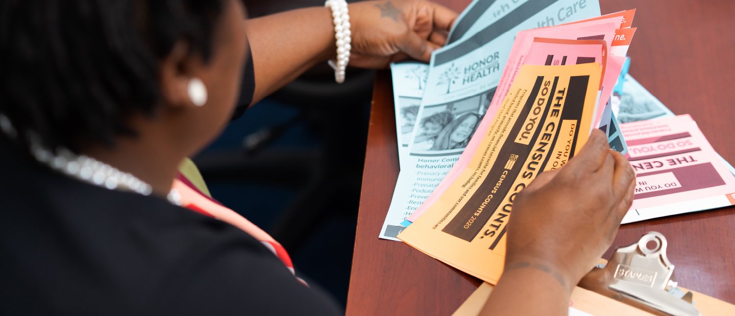 A woman seated at a table, looking through Census and health care flyers.