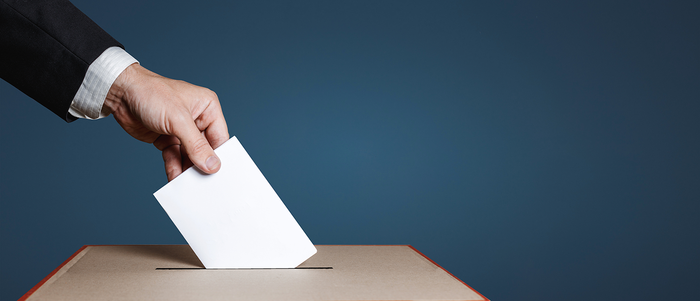 A hand placing a ballot into a box.