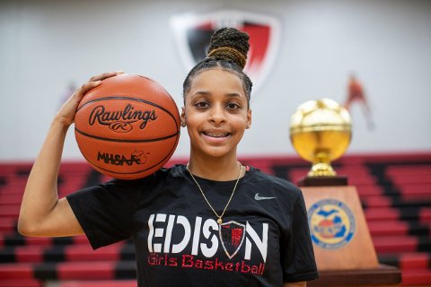 Damiya Hagemann holding a basketball on her shoulder, standing in front of a trophy, smiling at the camera