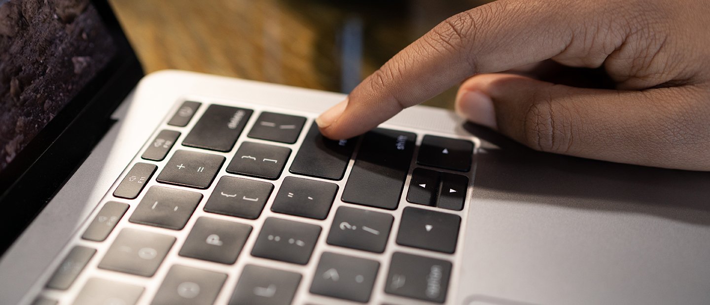 A finger pressing the "enter" key on a laptop.