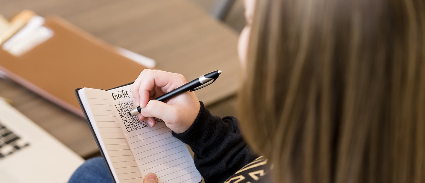 An Oakland University student making check marks next to courses listed in a notebook.