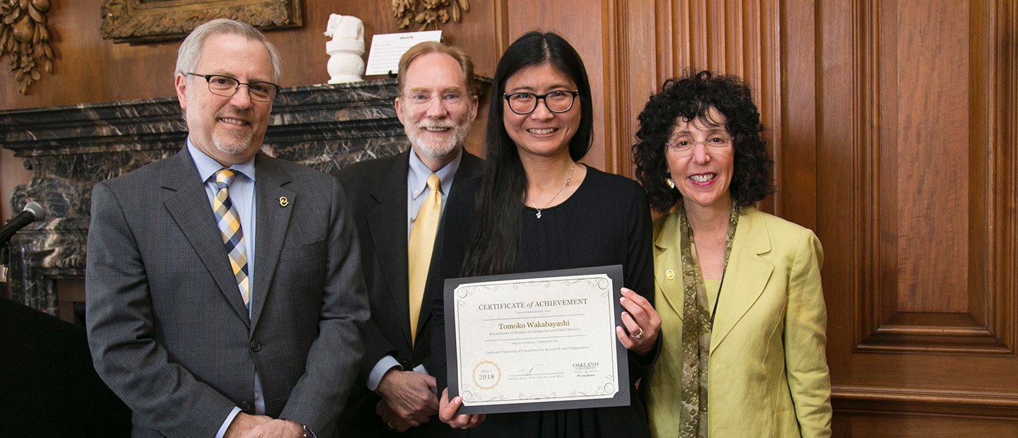 Four people posing for a group photo. One woman is holding a certificate.