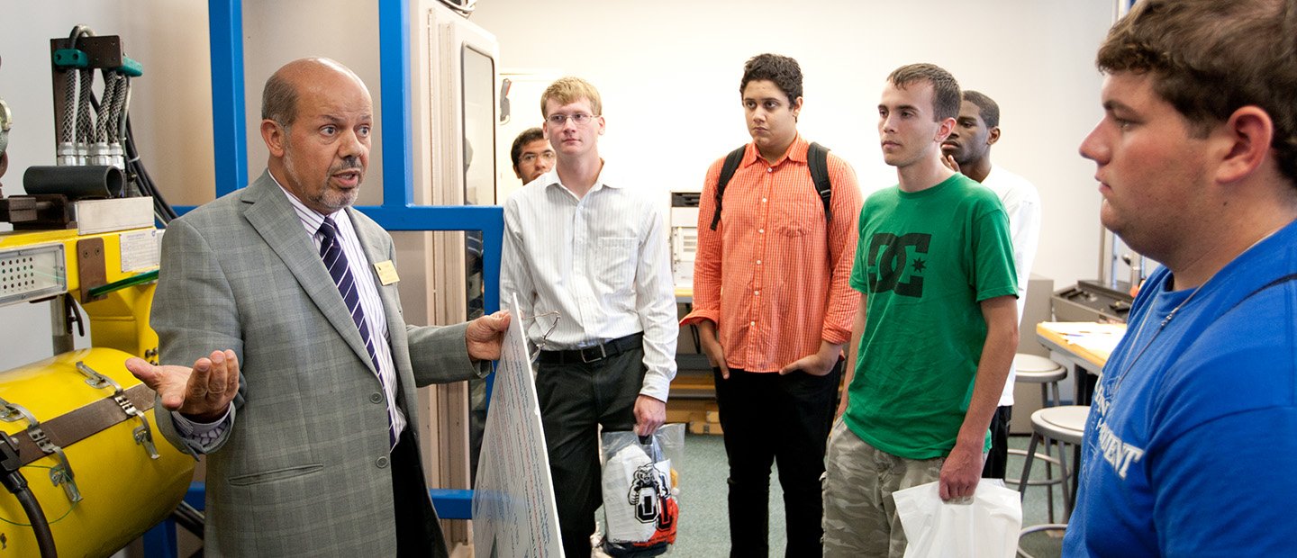 A professor talking to a group of students in a research lab.
