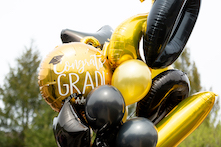 image of various sizes of black and gold balloons, one has the text "congrats grad!" on it