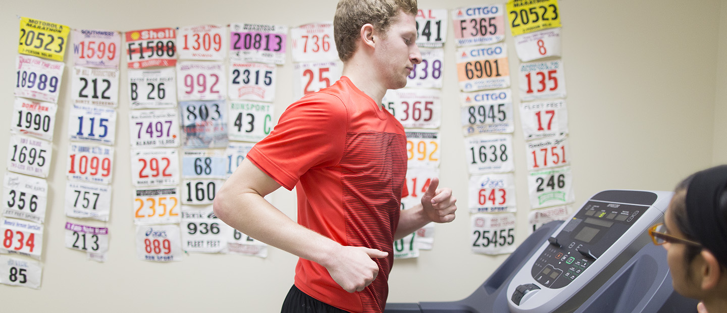 image of a person running on a treadmill with a second person monitoring the treadmill statistics