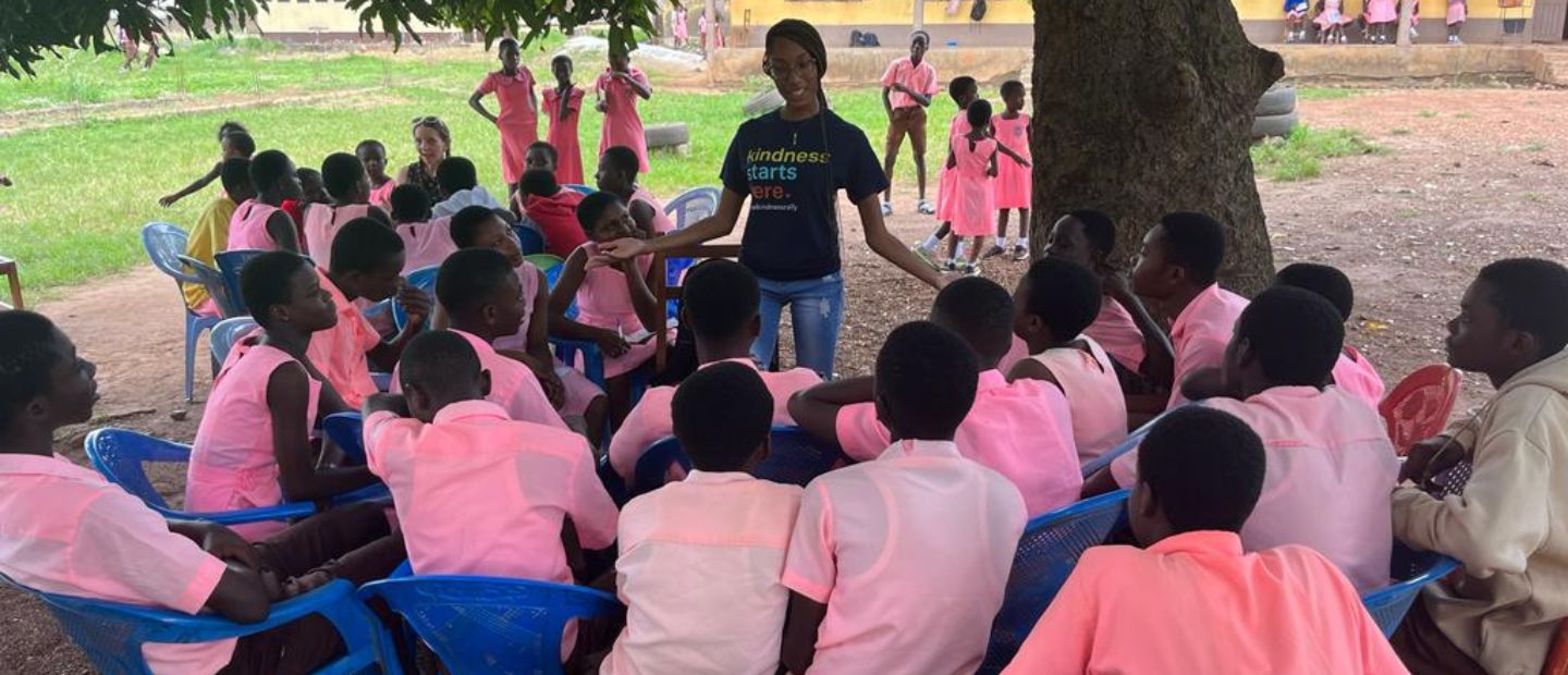 A woman speaking to a group of kids in pink shirts outside.