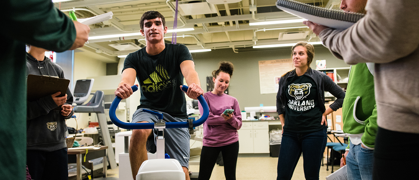 image of a man riding a stationary bike in a lab while people watch and take notes
