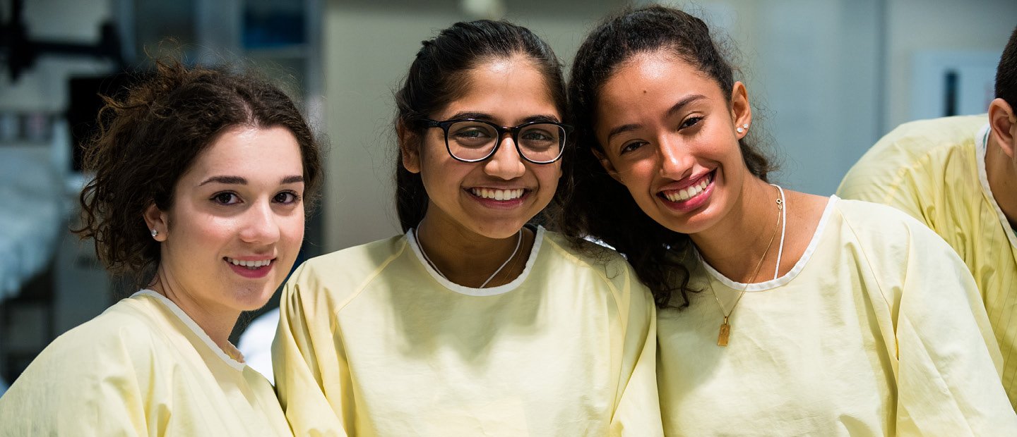 three female students in yellow lab coats