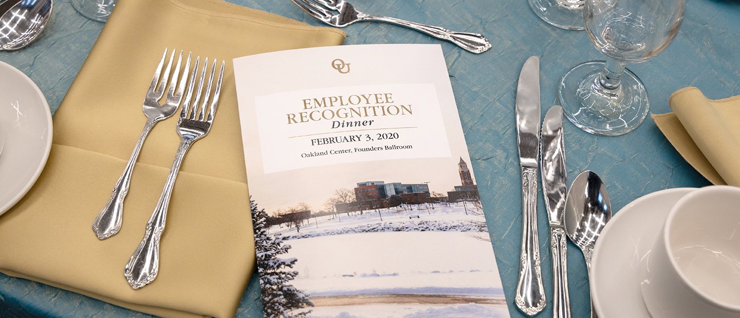 A place setting at a dining table with a program for the Employee Recognition Dinner event.