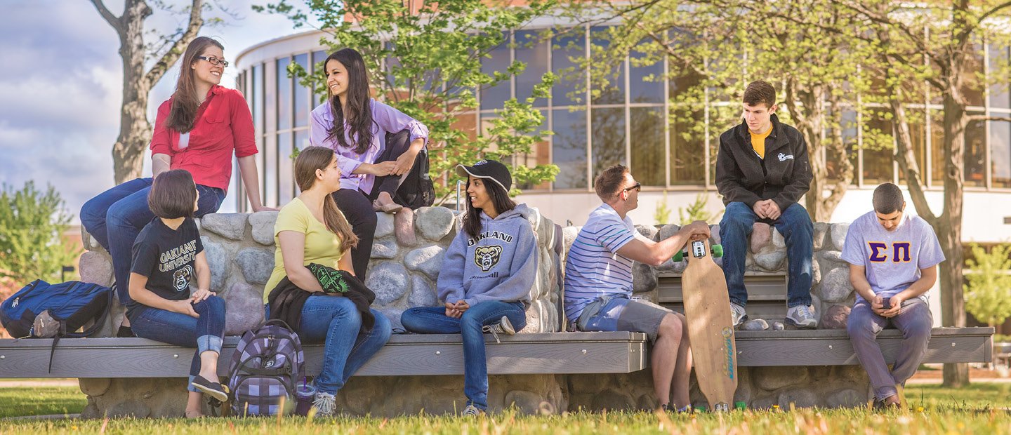 A group of students seated on benches outside, talking and smiling.