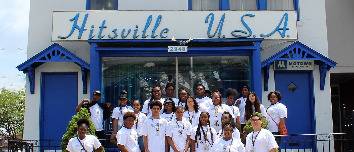 A group of students posing for a photo outside of a Motown building with a sign that says "Hitsville U.S.A."