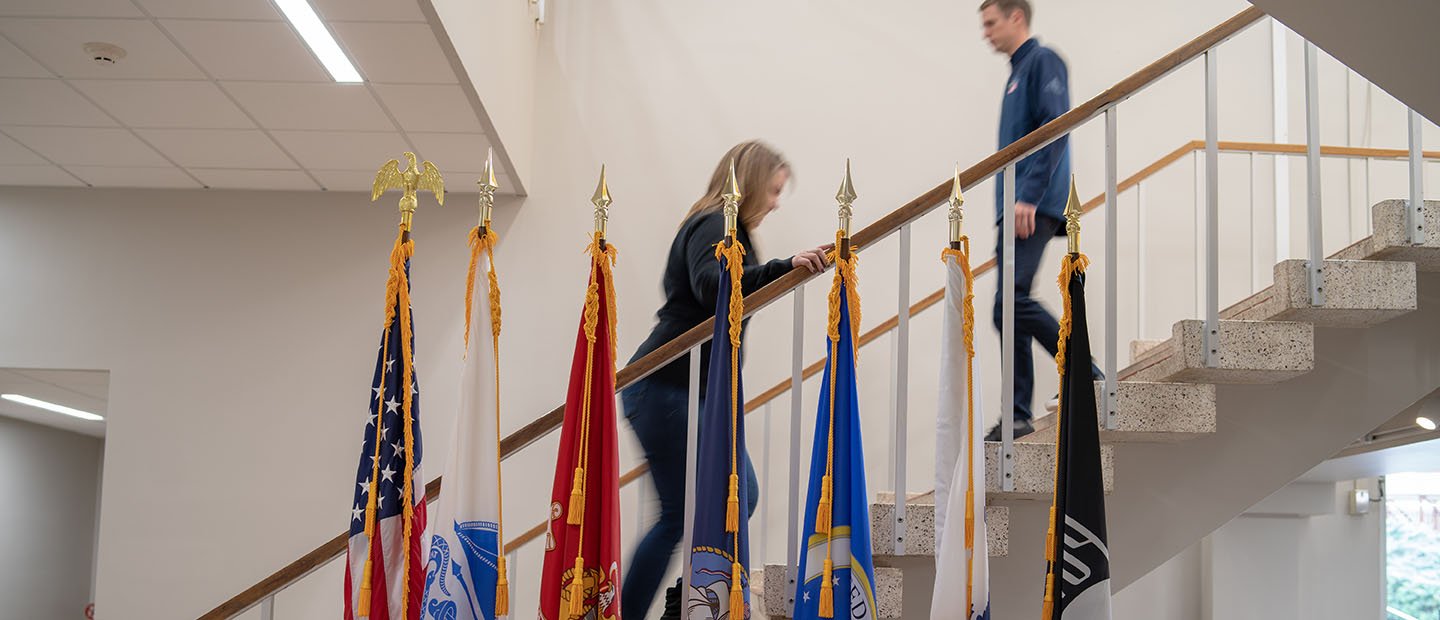 two people on a stairway behind a row of flags