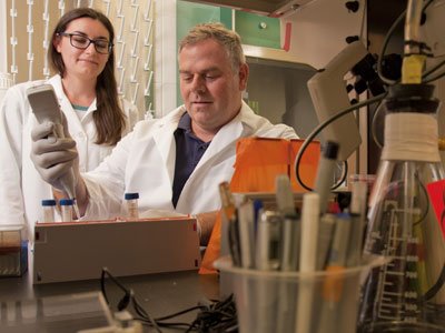 Man and Woman wearing white coats and working on an experiment in an a lab.