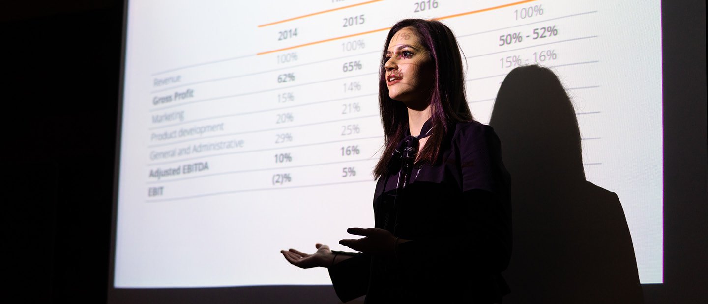 A young woman standing in front of a projector screen displaying percentage data.