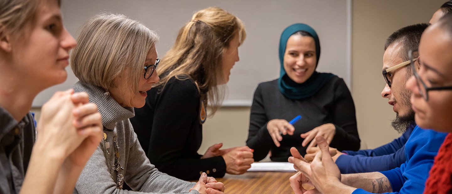 A group of adults seated at a rectangular table, having a conversation.