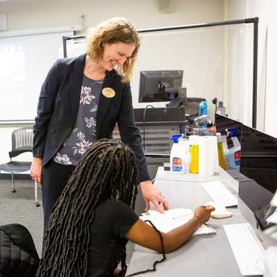 A smiling woman talks to a student seated at a table.