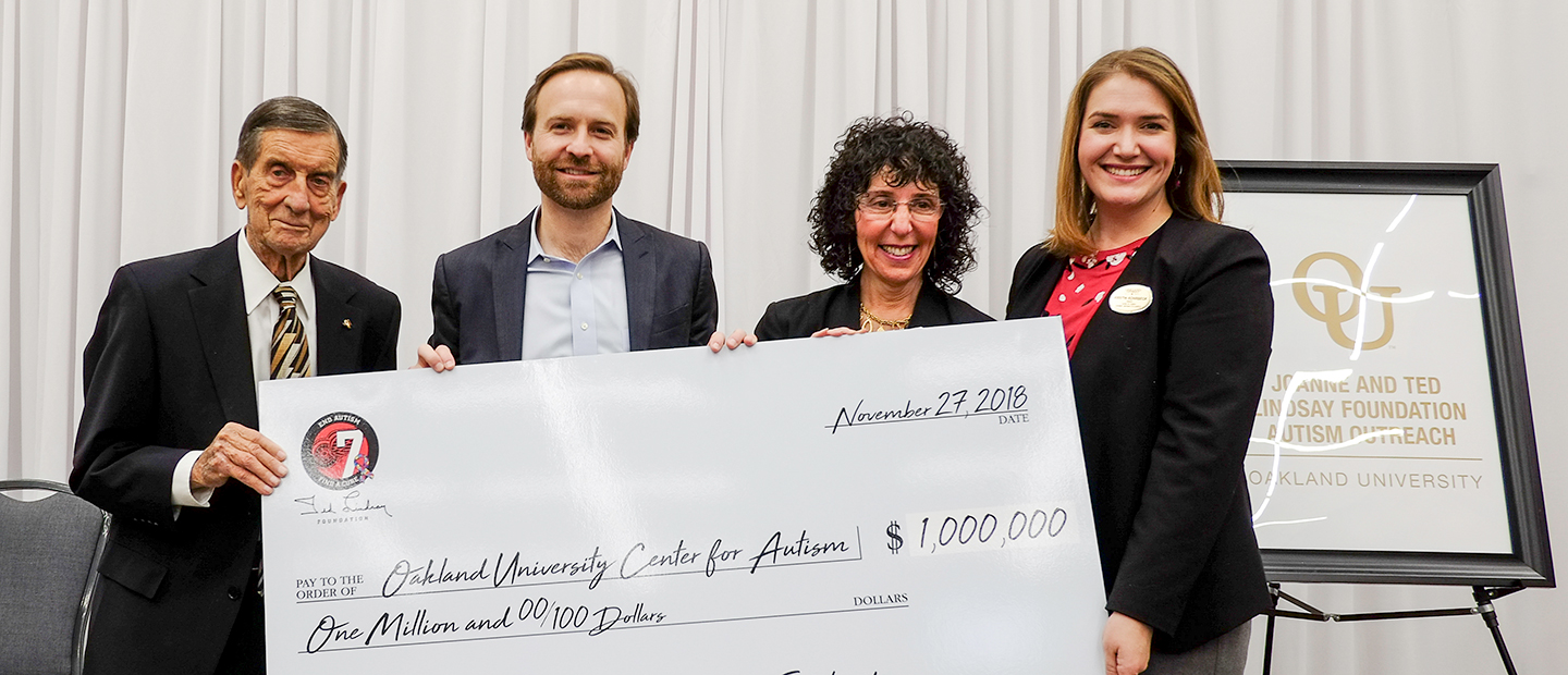 Four people holding a large check for the Oakland University Center for Autism