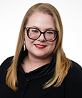 Headshot: Long Blonde haired woman with Glasses and black Suit jacket and blue top smiling at the camera.