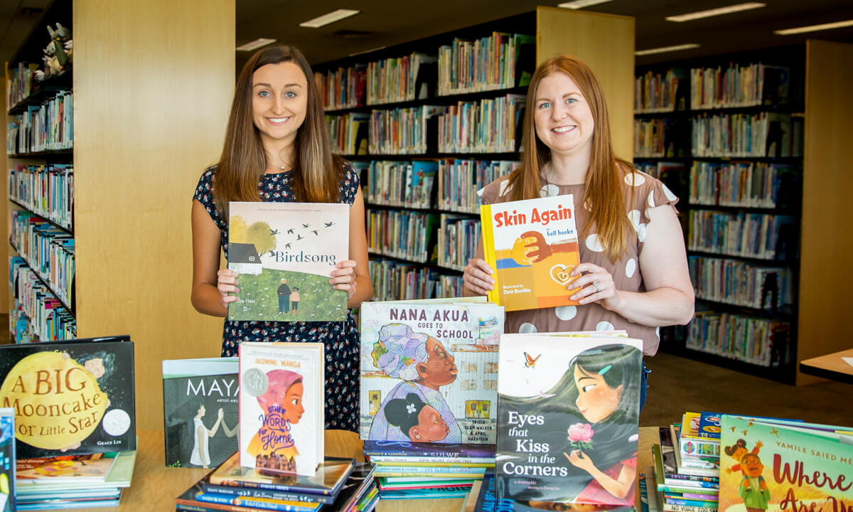 Two college students standing with stacks of books in a library