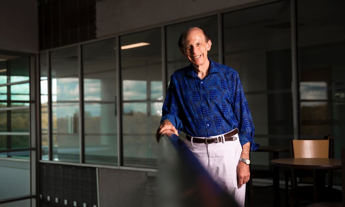 Man stands against a railing inside a campus building.