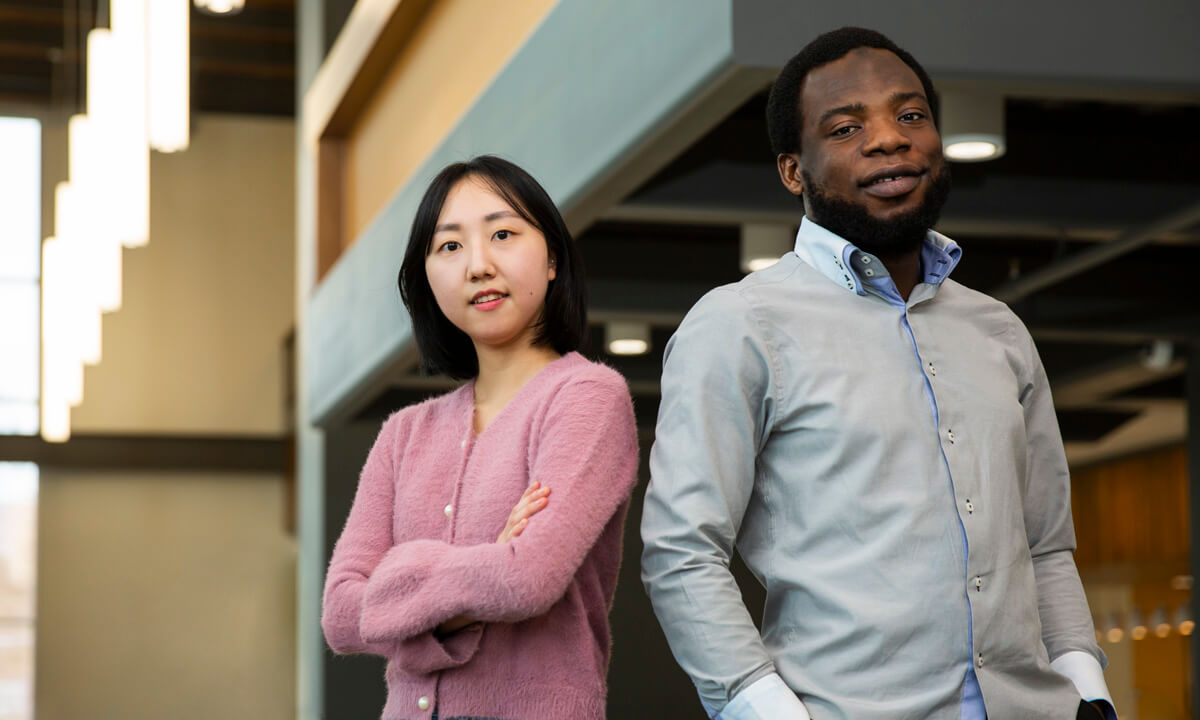 A college-aged woman standing next to a college-aged man both looking at the camera smiling.