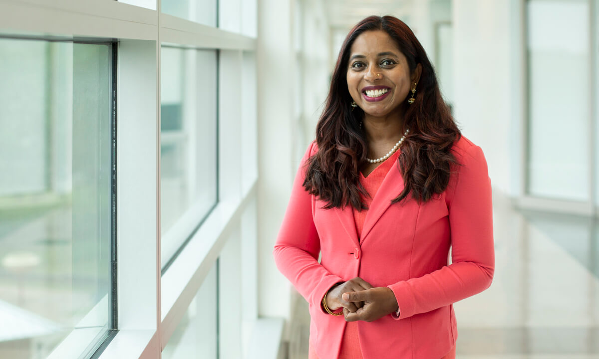 A smiling female professor standing in a bright hallway