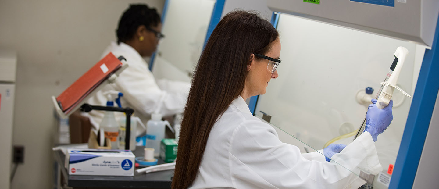 two women wearing white coats, using equipment in a lab