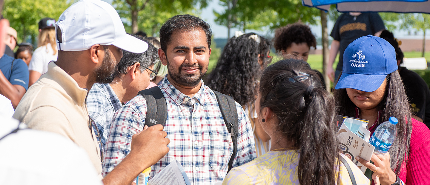 A young man wearing a backpack stands with a group of people smiling