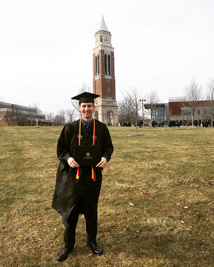 Michael Maguran is seen in his cap and gown in front of Oakland's clock tower.