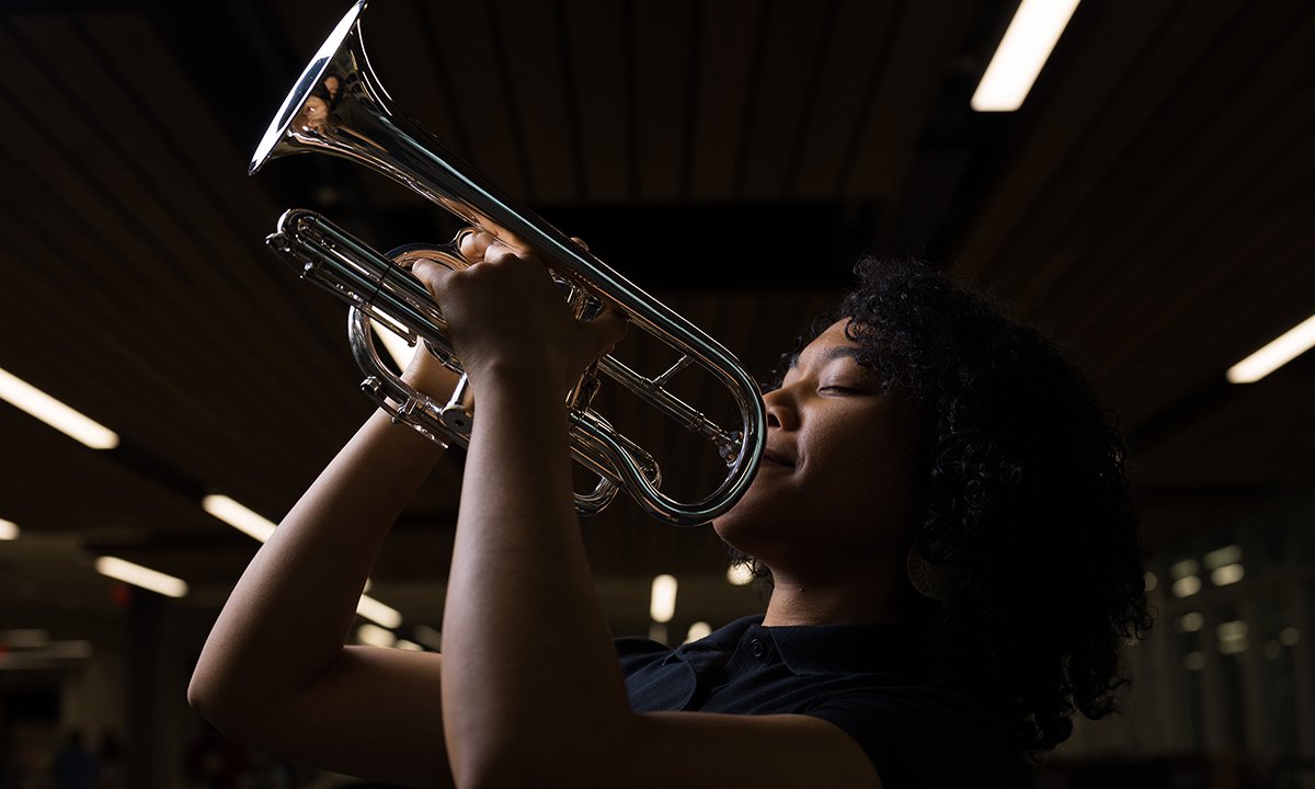 Woman holding a trumpet smiles at the camera.