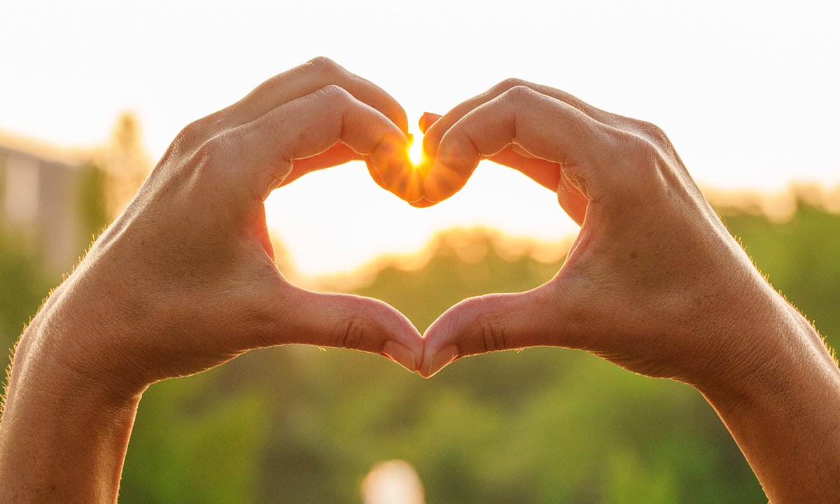 Hands together to form a heart around a sun setting