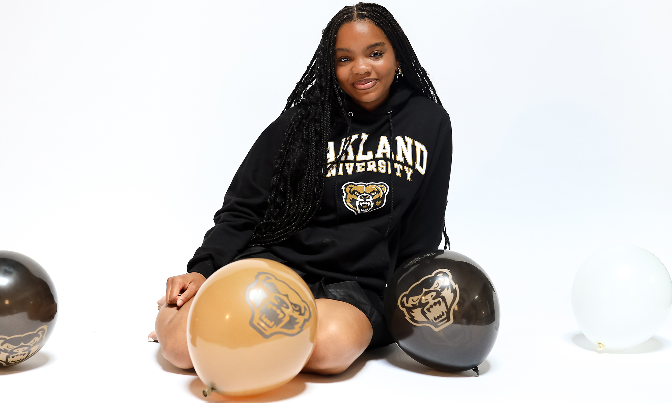 Mercy Jeffries sits on the ground next to Oakland University themed balloons.