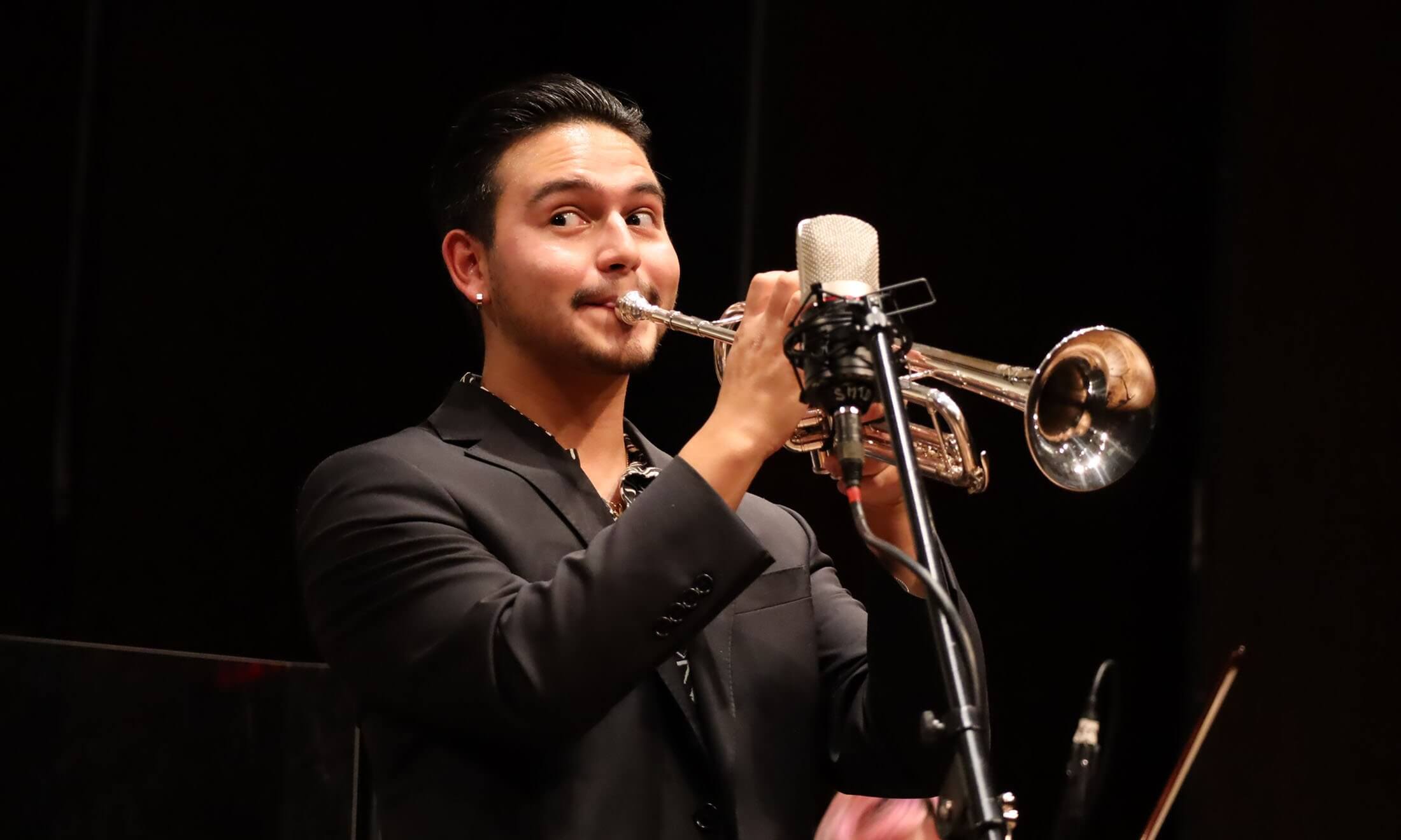 A man playing the trumpet on stage in front of a microphone.