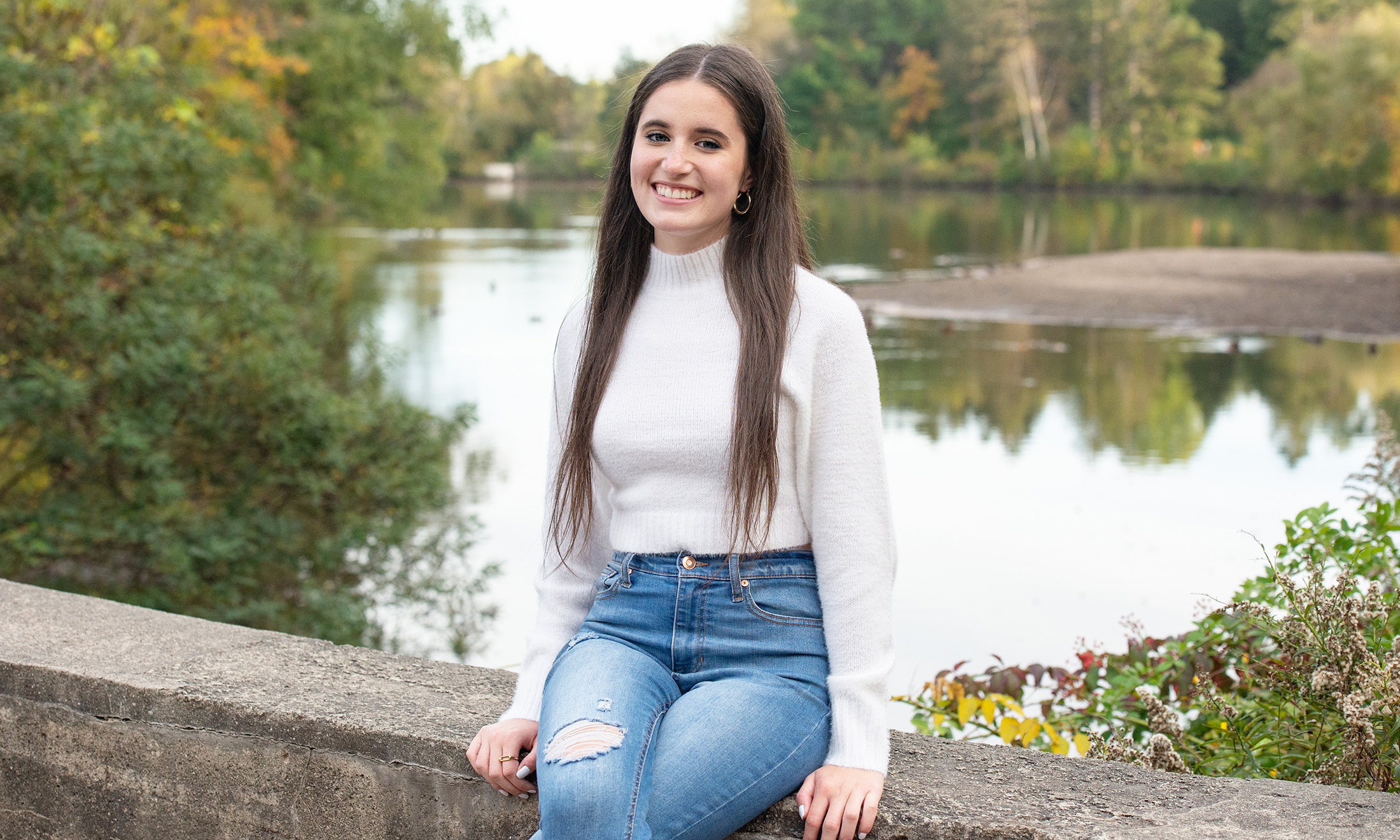 Emily Smeu sits on cement bench in front of a pond.