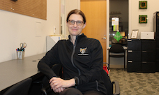 A smiling woman in O U jacket sits in an office.