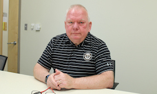 A man in an Oakland University polo shirt sitting at a desk.