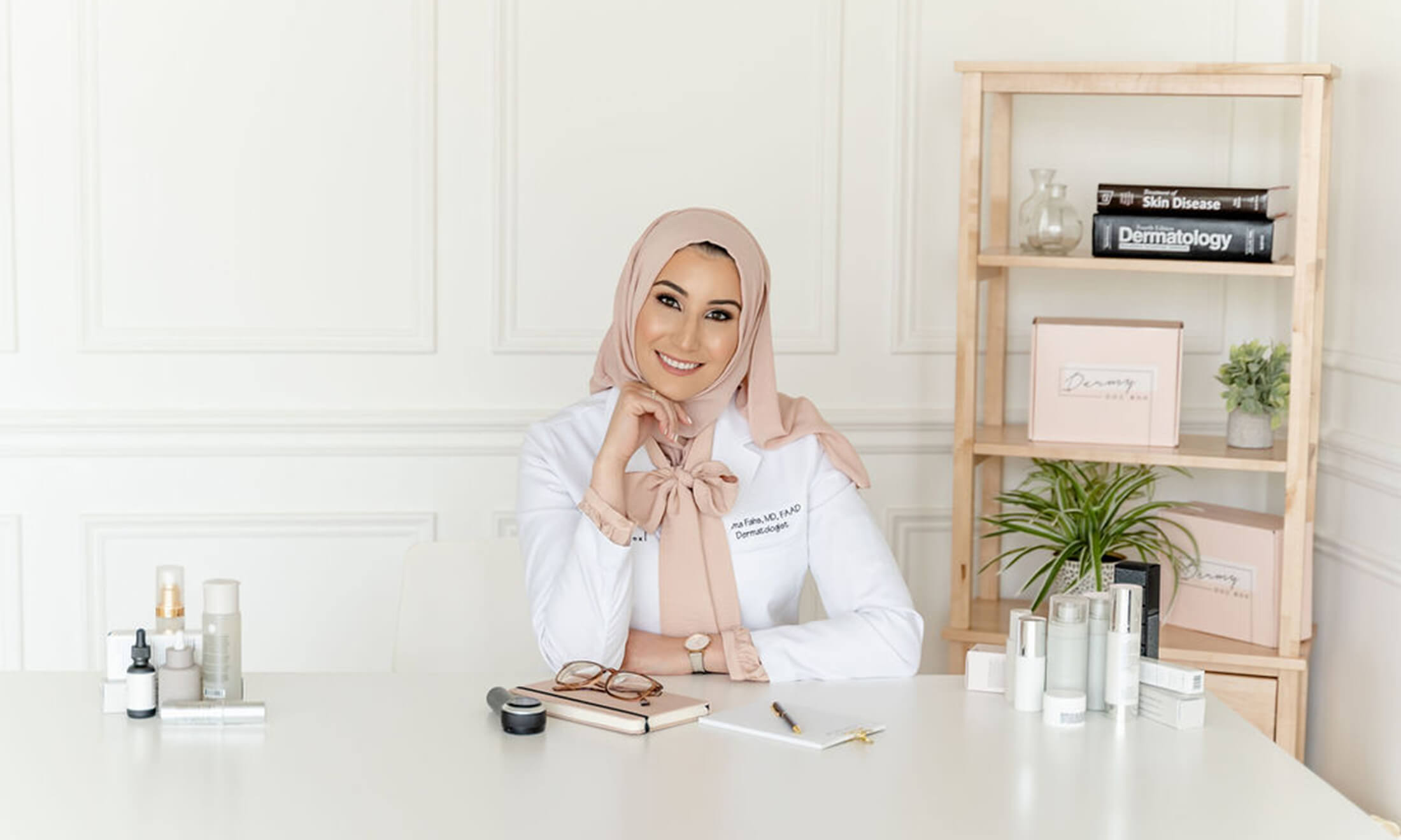 Woman in medical coat sits at desk smiling at the camera.