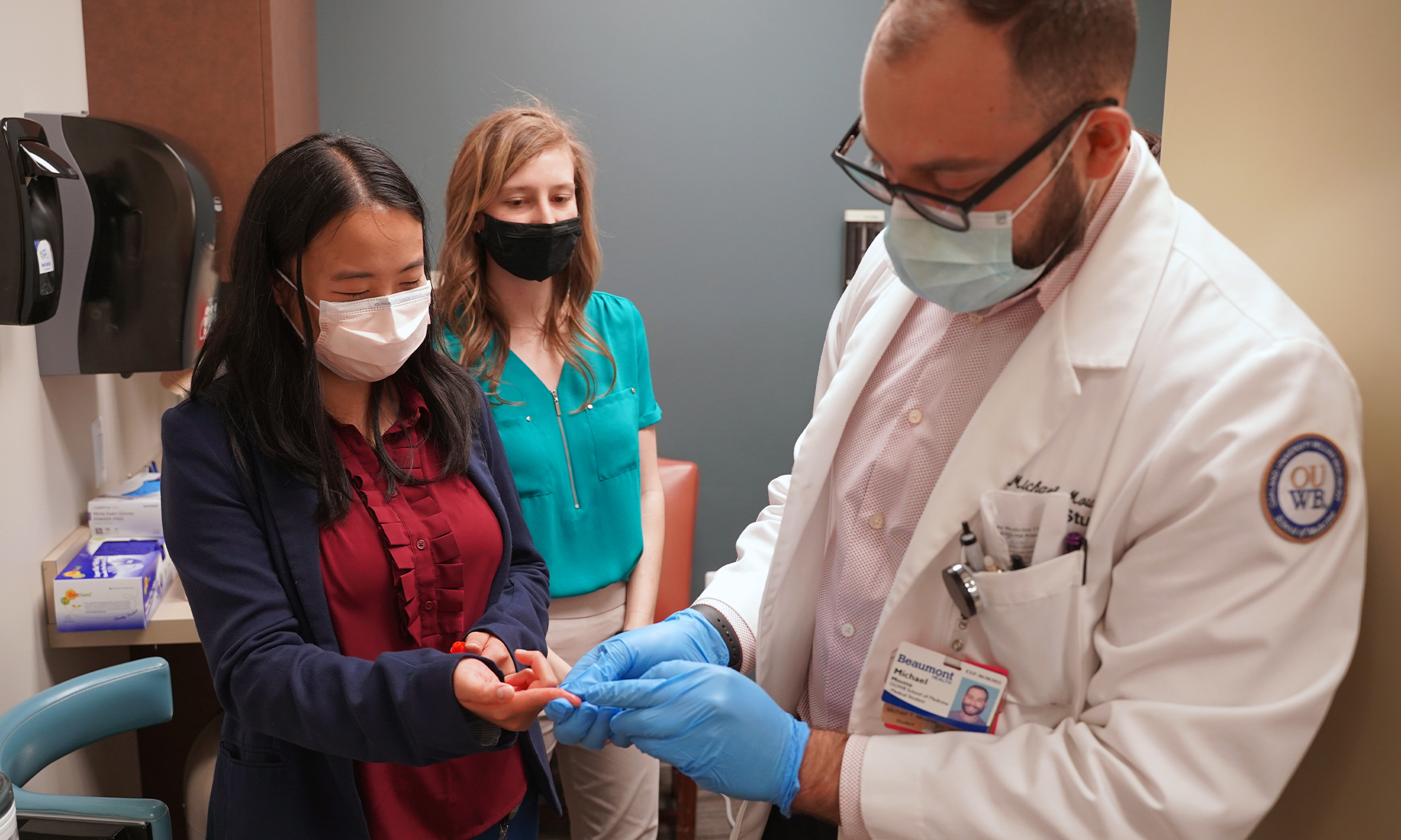 Michael Moussa (right), Tiffany Loh (left), and Sarah Provencher (center) demonstrate a finger stick blood test for volunteers