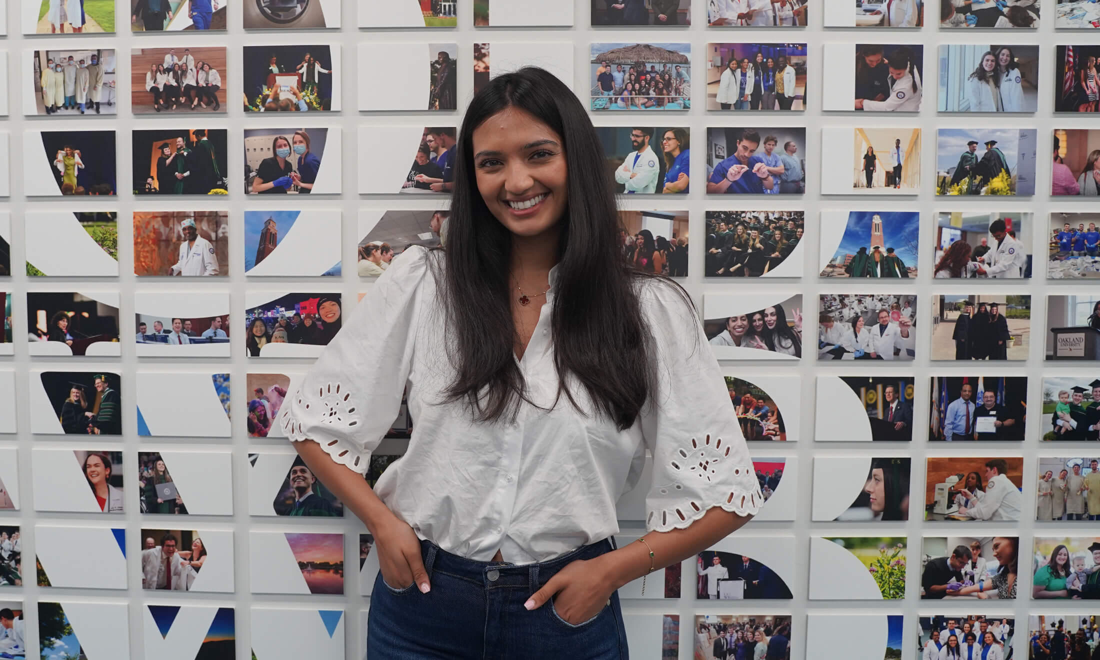 An image of a student smiling in front of a photo wall