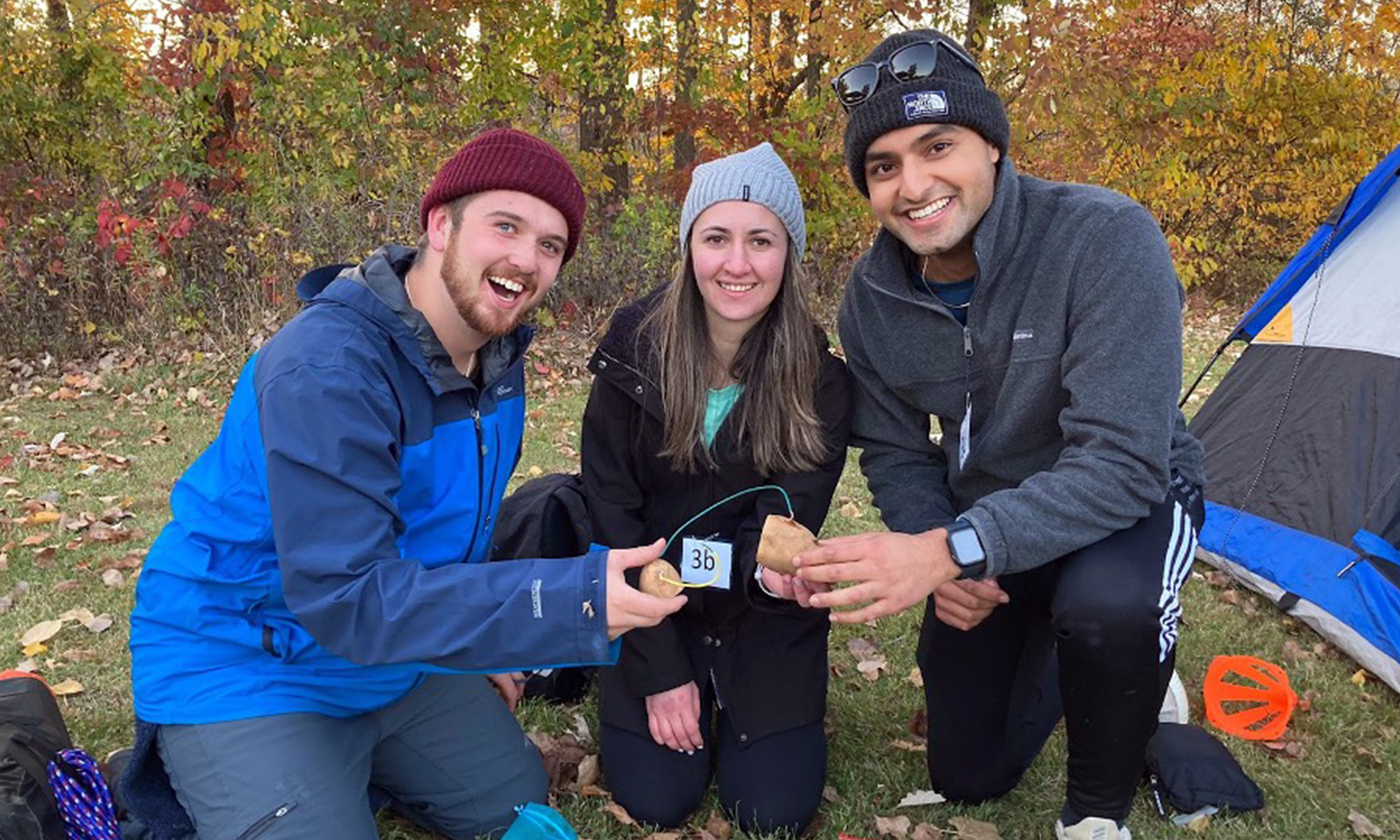 Three students wearing outdoor gear smile at the camera